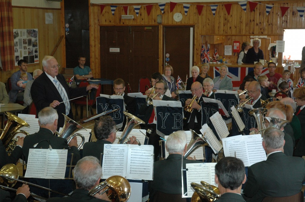 Silver band playing in doors lead by a conductor.