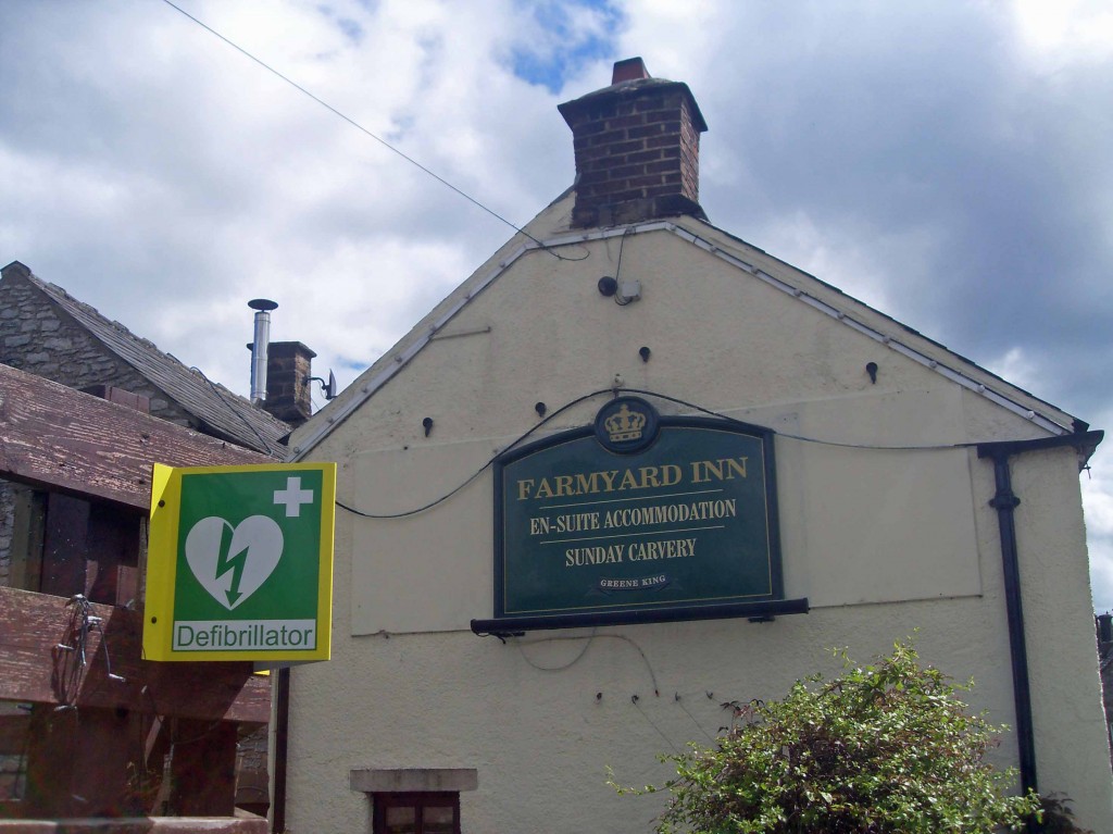 External view of a pub and sign 'Farmyard Inn' near another sign saying defibrillator.