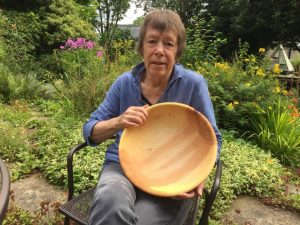 An image of a woman sat in a garden holding a hand made wooden bowl.
